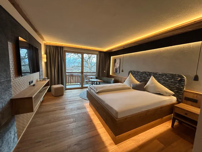 Moderna camera d'hotel con pavimento in legno, letto matrimoniale, vista balcone e luce calda